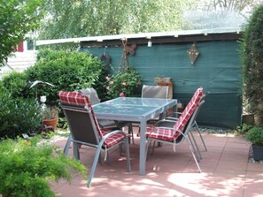 Une terrasse extérieure avec une table et des chaises, entourée de verdure et d’un mur végétal.