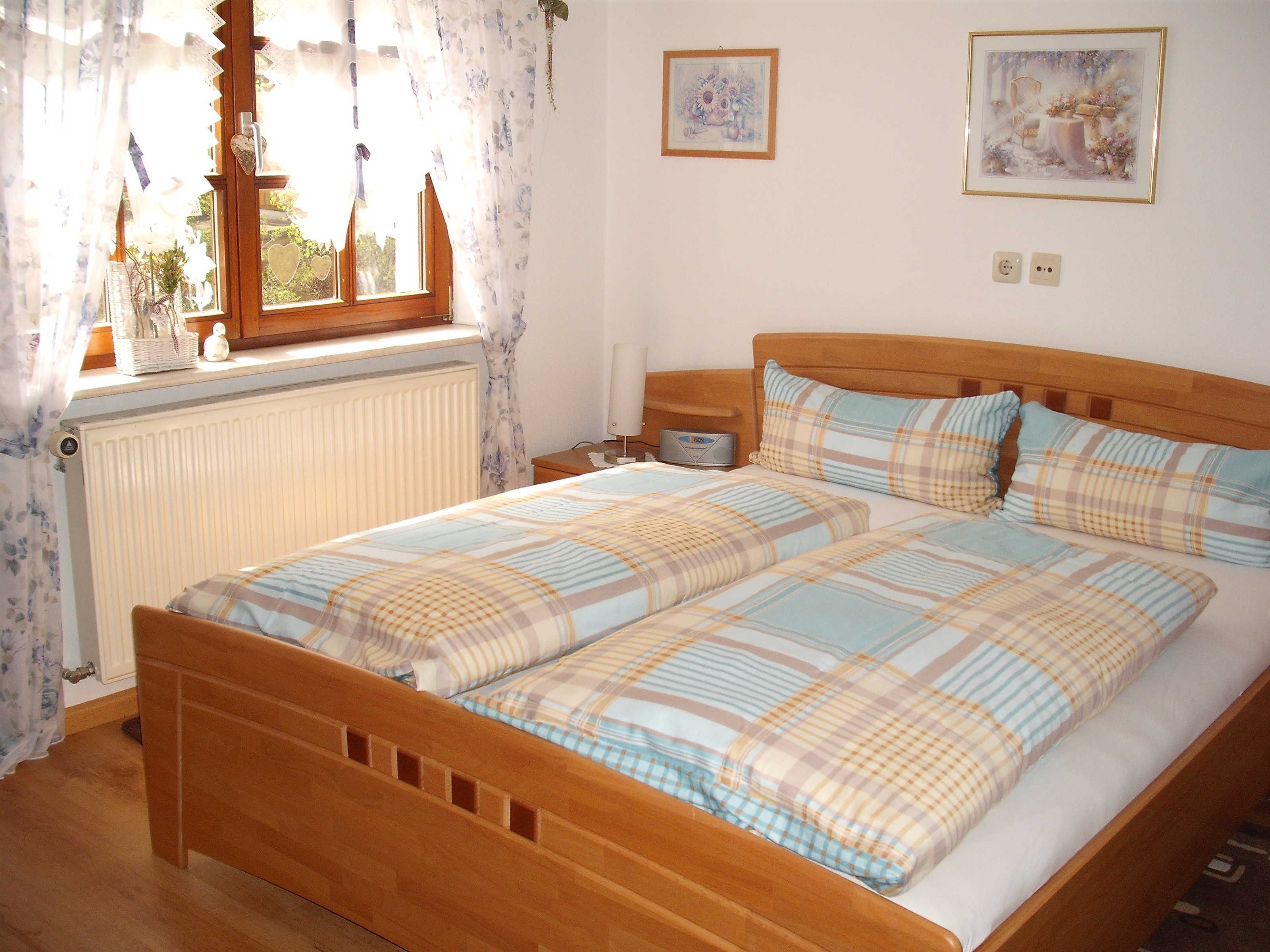 Une chambre à coucher avec un lit en bois, deux tables de chevet, un radiateur et une fenêtre avec des rideaux.