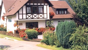 A traditional half-timbered house with a pitched roof, a front porch, and a well-maintained garden with various plants and flowers.