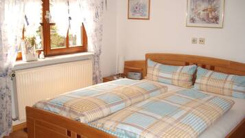 Une chambre à coucher avec un lit en bois, une fenêtre avec des rideaux, un radiateur et deux tableaux encadrés accrochés au mur.
