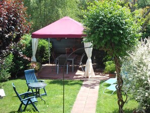 Un espace patio avec un parasol rouge, deux chaises bleues et une table.