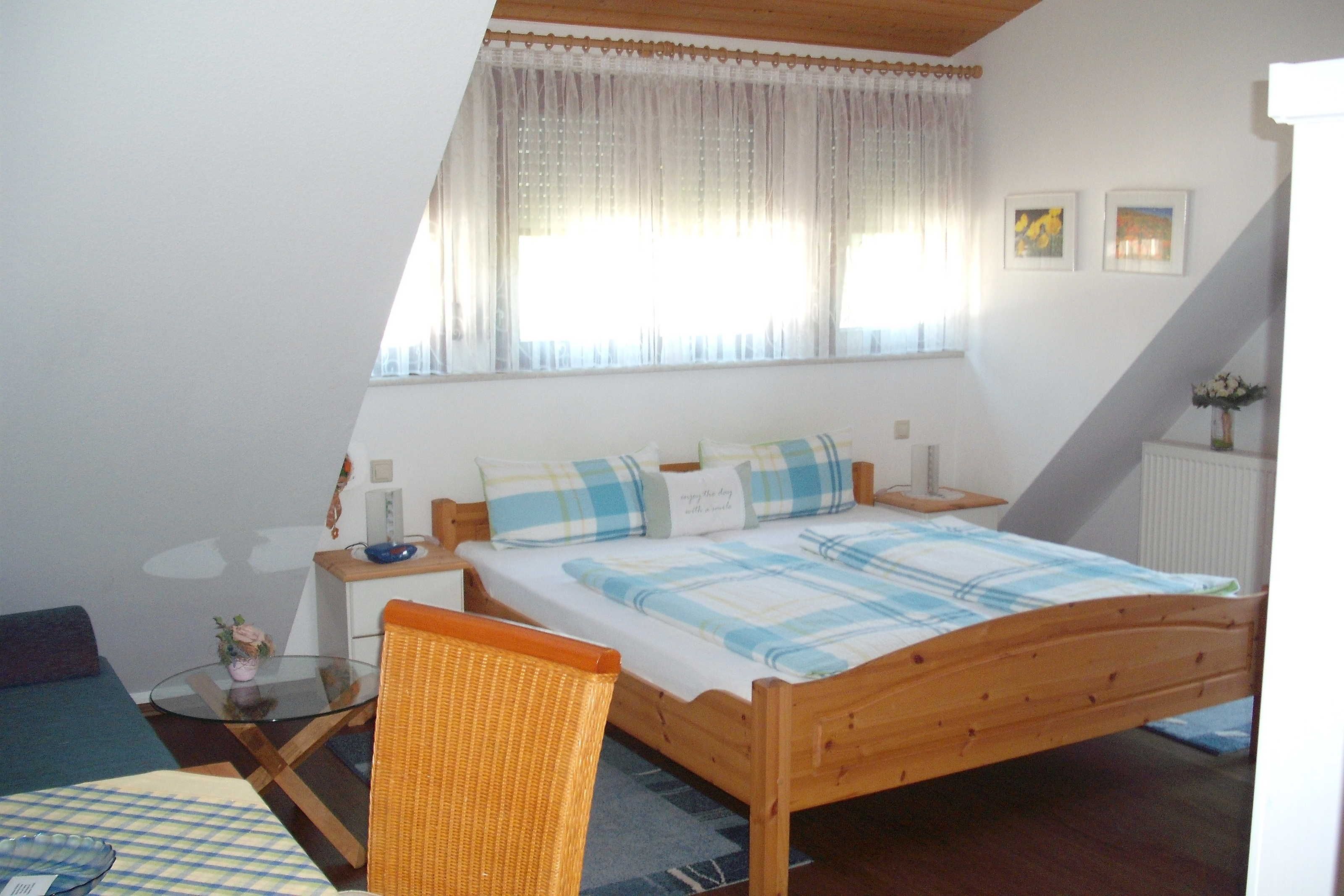Une chambre à coucher comprenant un lit, une chaise, une table, une fenêtre avec des rideaux et un radiateur.
