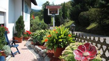 Un bâtiment avec une enseigne indiquant qu’il s’agit d’une maison d’hôtes, un chemin piétonnier dallé et une variété de plantes et de fleurs en pot.