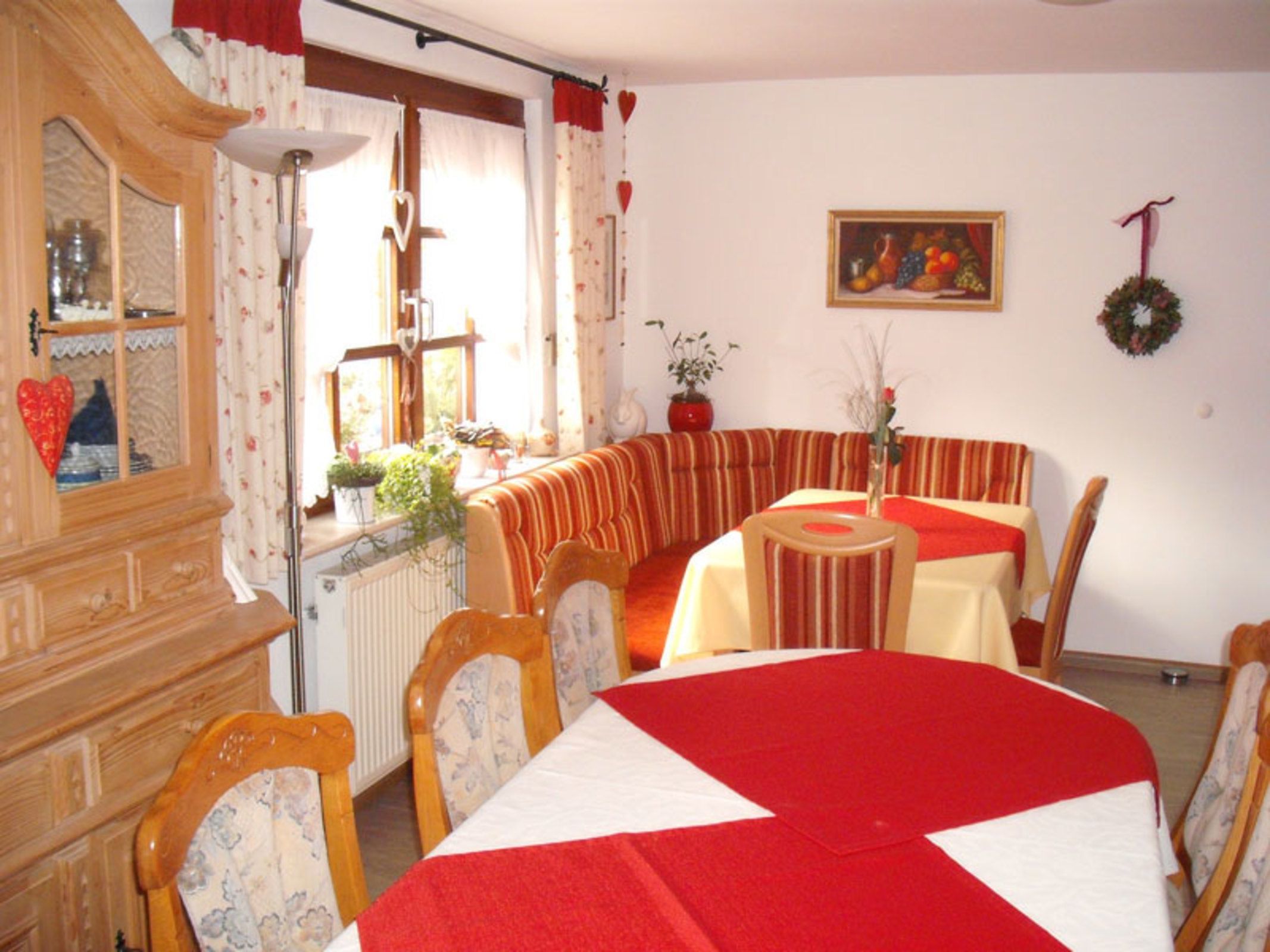 Ein Essbereich mit Tisch, Stühlen, einem Heizkörper, einem Schrank und einem Fenster mit Vorhängen.