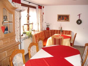 Un coin repas comprenant une table, des chaises, un radiateur, un meuble et une fenêtre avec des rideaux.