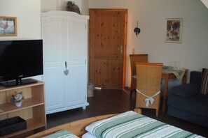 A room with a television, a wardrobe, a dining table with chairs, and a sofa. - Double room with WC and shower (forest side) Das Kleine FEINE - Guesthouse (Ettenheim)