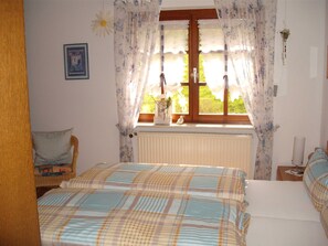 A bedroom with a bed, a chair, a window with curtains, a radiator, and a bedside table with a lamp. - Double room with WC and shower (forest side) Das Kleine FEINE - Guesthouse (Ettenheim)
