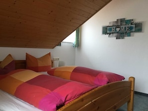 A bedroom with a wooden ceiling, a bed with multicolored bedding, and a wall decoration with the word "HOME".