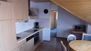 A compact kitchen with wooden cabinets, a built-in oven, and a microwave on a shelf. - Vacation apartment Hardtblick 70sqm, 2 bedrooms, max. 4 pers. - Haus Fechtig (Bonndorf im Schwarzwald)