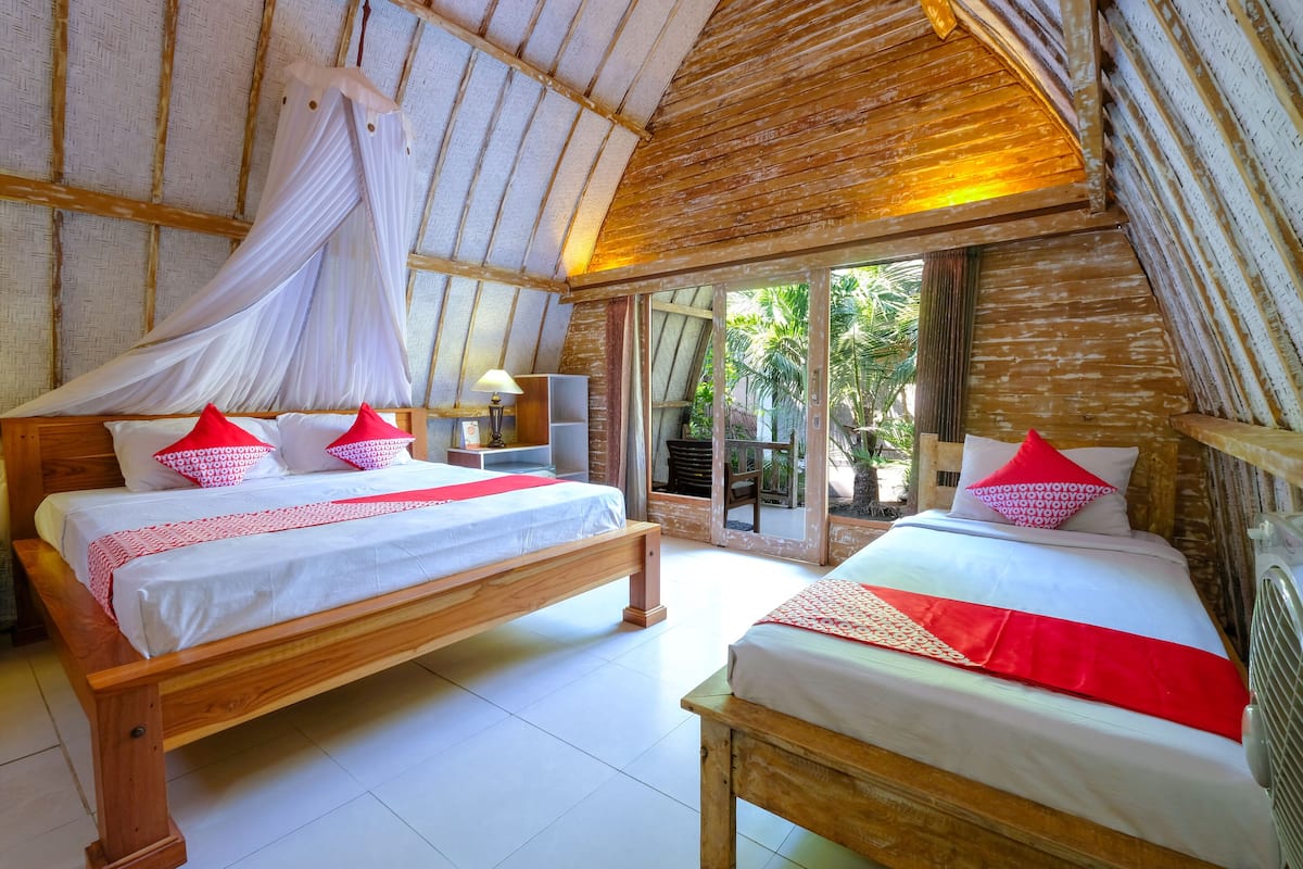 A bedroom with two wooden beds, white bedding, red pillows, and a canopy bed.