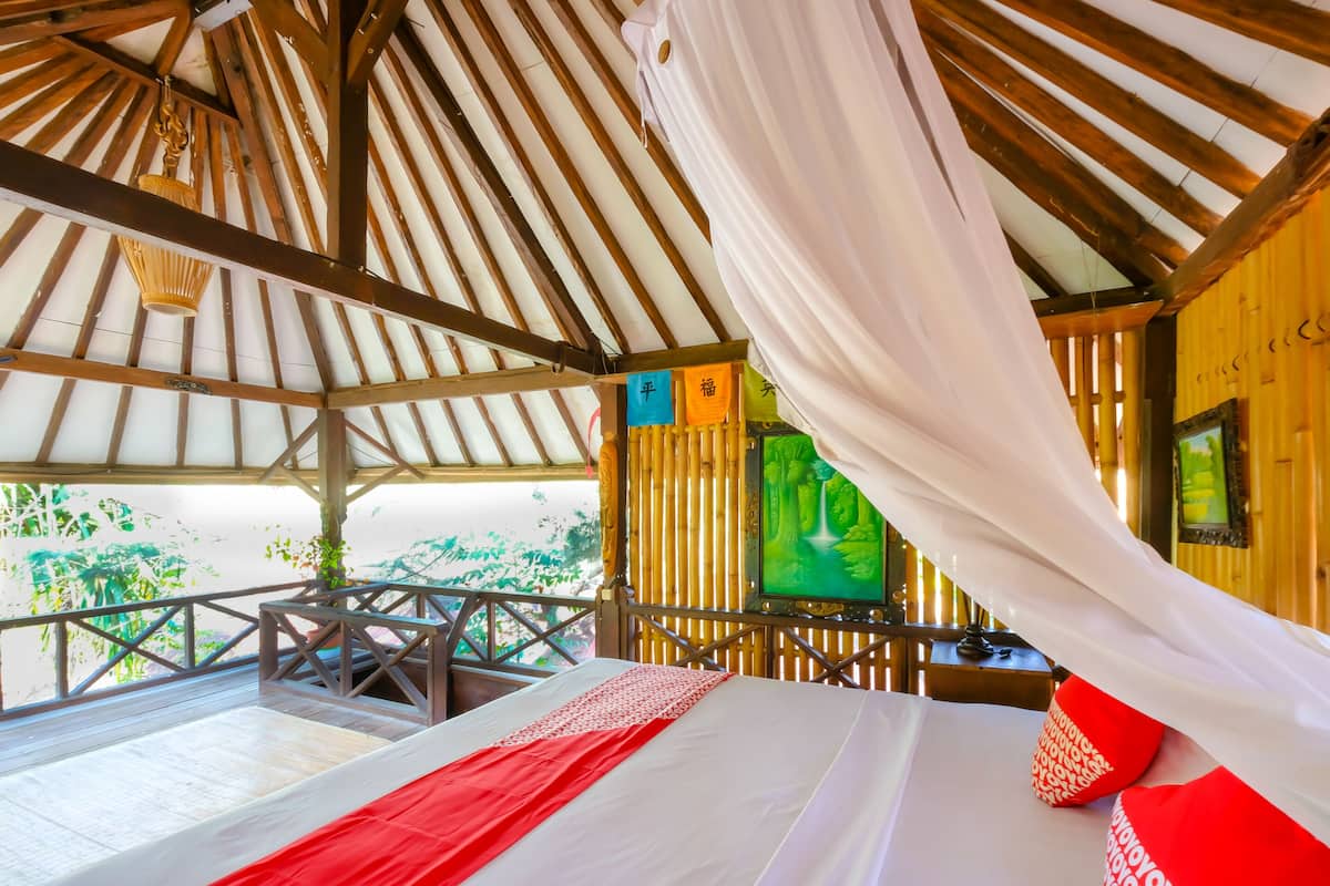 A room with a bed, a wooden ceiling, and a view of greenery outside.