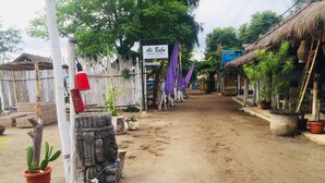 A dirt path leading to a rustic building with a thatched roof, surrounded by potted plants and a bamboo fence. - Alibaba Bungalows (Gili Air)