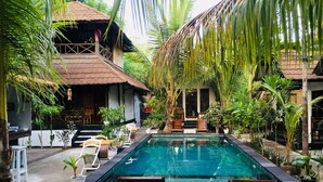 A pool area with lounge chairs and a small table, surrounded by lush greenery and a thatched-roof structure. - Alibaba Bungalows (Gili Air)