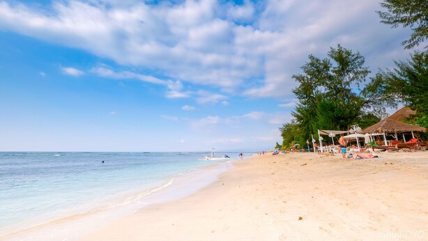 A beach with clear skies, calm waters, and a few people. There are umbrellas and a thatched-roof structure. - Alibaba Bungalows (Gili Air)