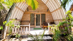A wooden structure with a sloped roof, large glass doors, and a wooden porch with a bench. - Alibaba Bungalows (Gili Air)