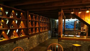 A cozy restaurant with a stone wall and wooden shelves displaying bottles. There is a round table with chairs and a decorative item on it. - Karauzumler Konagi (Safranbolu)