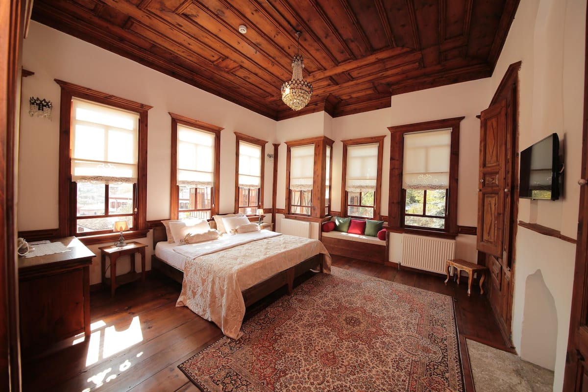 A spacious bedroom with a large bed, wooden ceiling, and multiple windows.