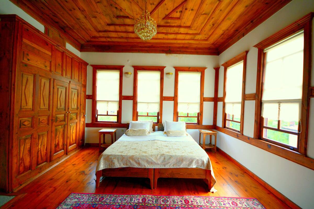 A bedroom with a large bed, wooden walls, and multiple windows.