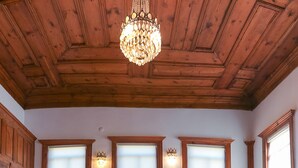 A room with wooden ceiling beams, two beds with matching headboards, a chandelier, and large windows with curtains. - Karauzumler Konagi (Safranbolu)