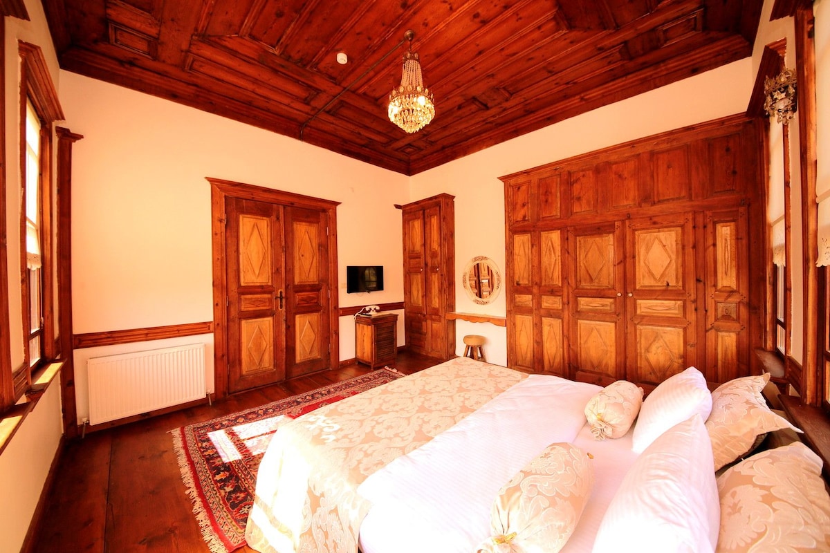 Un dormitorio con paneles de madera, un candelabro, una cama con ropa de cama floral y un televisor en la pared.