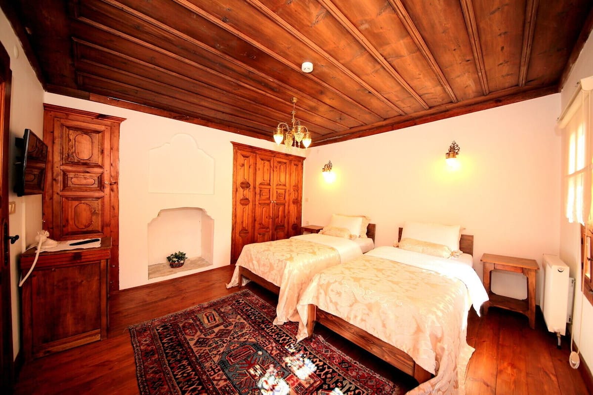 A room with two beds, a wooden ceiling, a fireplace, and a TV on a wooden cabinet.