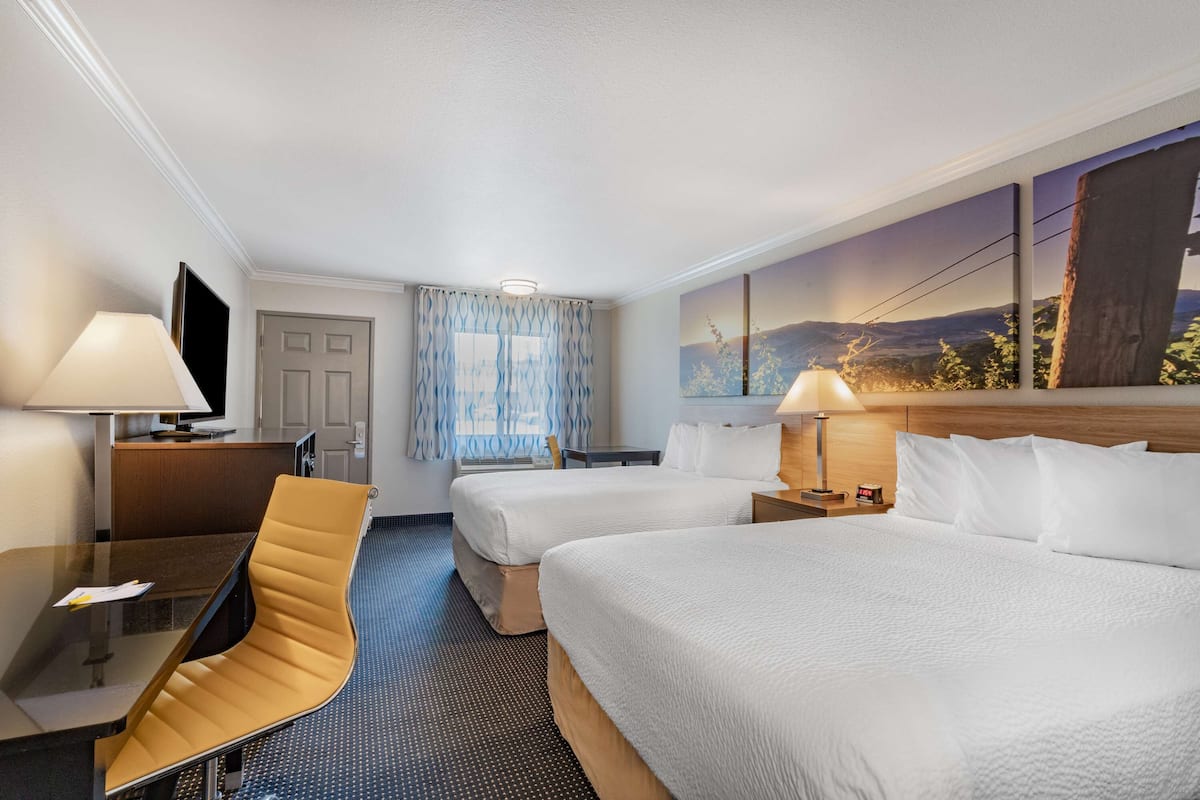 A hotel room with two beds, a desk, a chair, and a TV.