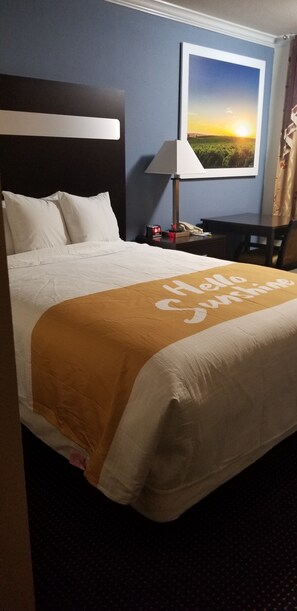 A hotel room with a bed, a nightstand, a lamp, a painting, and a chair. - Days Inn by Wyndham Winnemucca (Winnemucca)