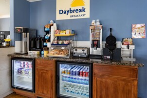 Un área de desayuno con un letrero Daybreak, un refrigerador con bebidas, una cafetera y un fabricante de gofres.