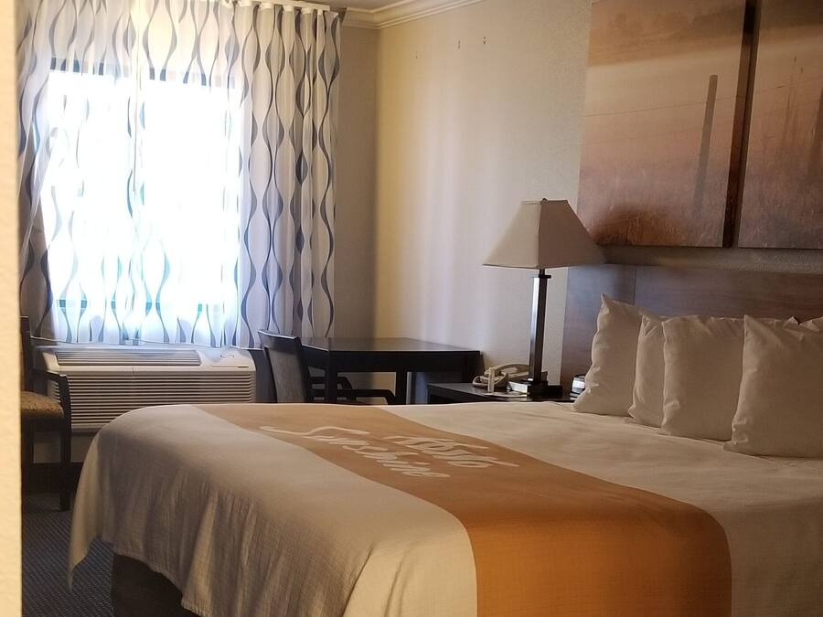 A hotel room with a large bed, a desk, a lamp, and a window with curtains.