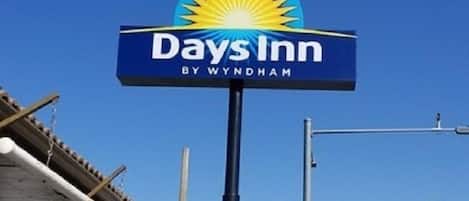Señal de Days Inn con un logo de sol y el texto 'Days Inn by Wyndham' contra un cielo azul despejado.