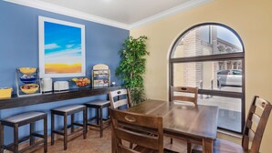 A dining area with a wooden table and chairs, a counter with bowls and a plant, and a large window with a view of the street. - Days Inn by Wyndham Winnemucca (Winnemucca)