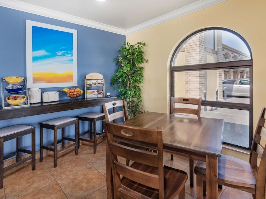 A dining area with a wooden table and chairs, a counter with bowls and a plant, and a large window with a view of the street.