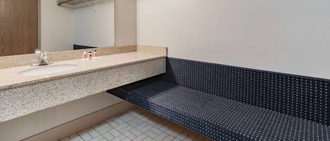 A bathroom with a granite countertop, a mirror, a wooden door, and a patterned bench.