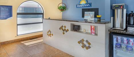 Un área de recepción con un reloj, un cartel de Days Inn, una planta pequeña, un refrigerador con bebidas y una ventana con vistas.