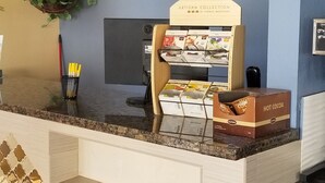 A reception desk with a Days Inn sign, a plant, a magazine rack, and a refrigerator. - Days Inn by Wyndham Winnemucca (Winnemucca)