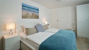A neatly arranged bedroom with a bed, bedside tables, and a painting of a beach scene. - 23 Ferienappartement Wittow (with balcony) - Apartment house Haus Arkona (Sellin)