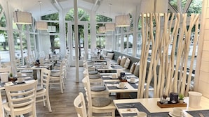A restaurant with white chairs and tables, a wooden floor, and hanging lights. - 23 Ferienappartement Wittow (with balcony) - Apartment house Haus Arkona (Sellin)
