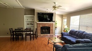 Una sala de estar con chimenea, un televisor montado encima, un sofá azul y una zona de comedor con sillas y una mesa.