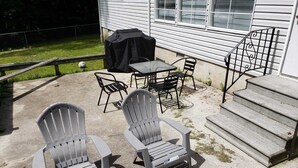 Un patio con dos sillas Adirondack, una mesa y una parrilla.