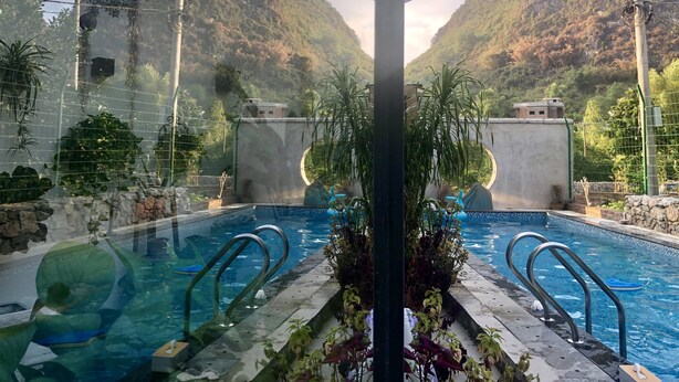 A swimming pool with clear blue water, surrounded by lush greenery and a mountainous backdrop. - Yangshuo Serene Cove Hotel (Guilin)