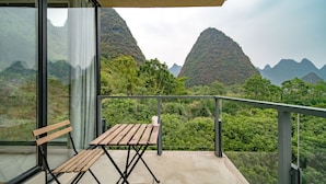 A balcony with a wooden table and bench, offering a view of lush green mountains. - Yangshuo Serene Cove Hotel (Guilin)
