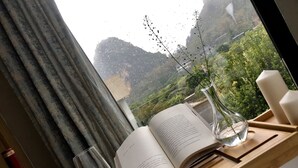 A table with a wine bottle, a glass, an open book, and a vase with plants. - Yangshuo Serene Cove Hotel (Guilin)
