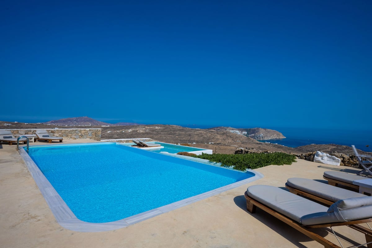 Una piscina con sillones de descanso y vistas al mar y las montañas.