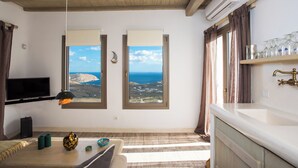 A room with a large window offering a view of the sea, a flat-screen TV mounted on the wall, a wooden ceiling, and a white sink with a brass faucet. - Amallini Suites Mykonos (Mykonos)