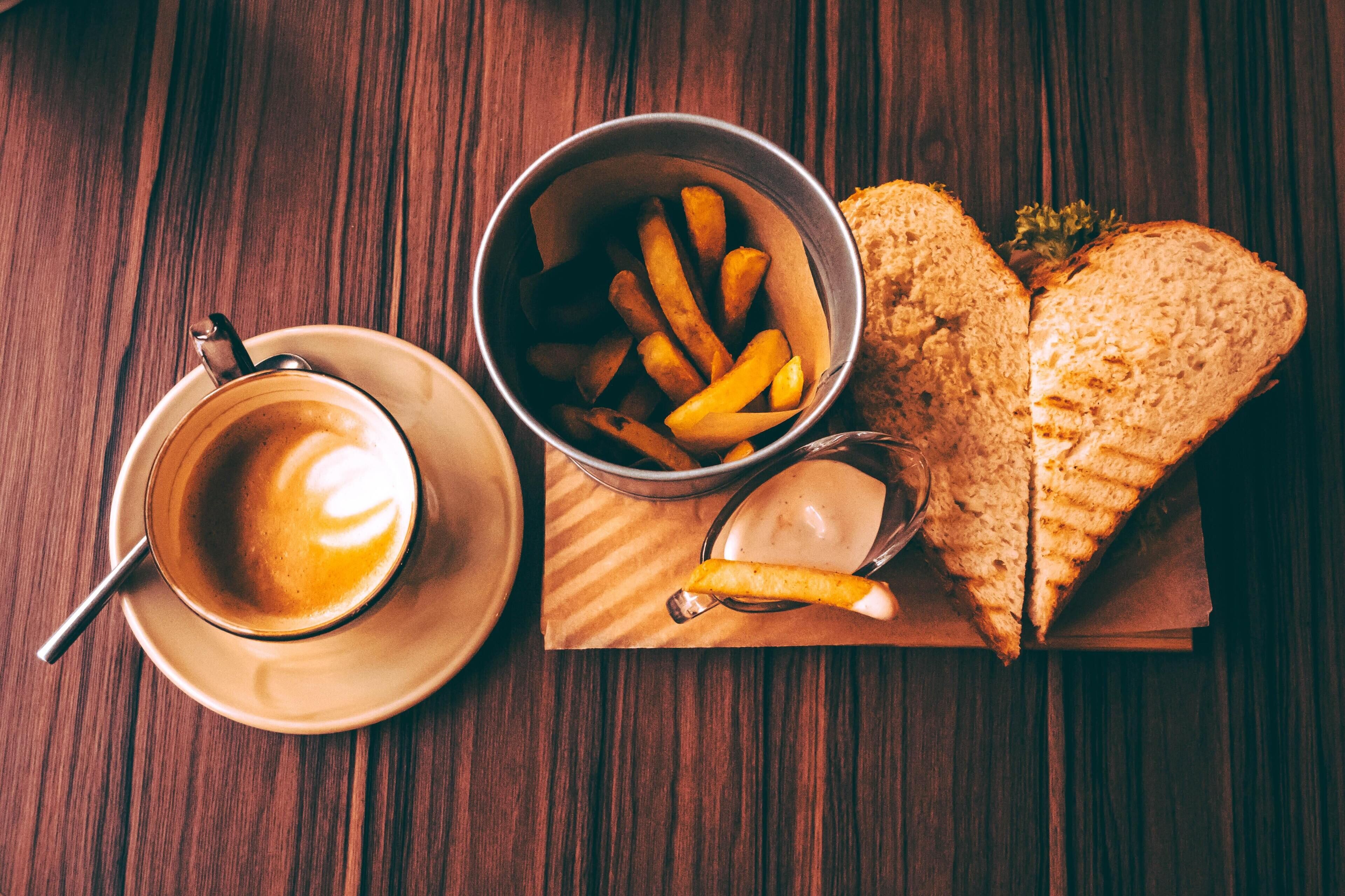 Ein Sandwich, Pommes und eine Tasse Kaffee auf einer Holztischplatte.