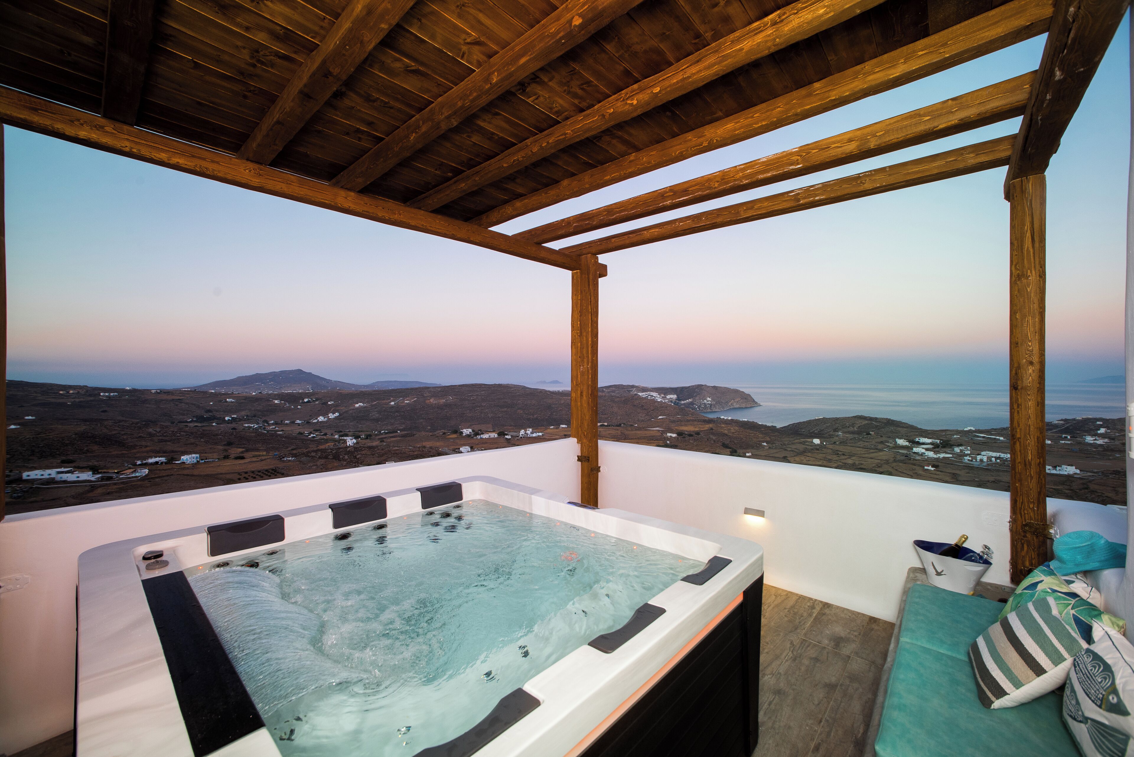 A hot tub under a wooden pergola with a view of a coastal landscape.