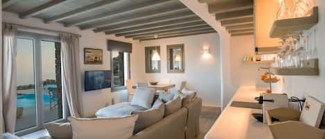 A modern living room with a sofa, a dining area with a table and chairs, and a view of a pool.