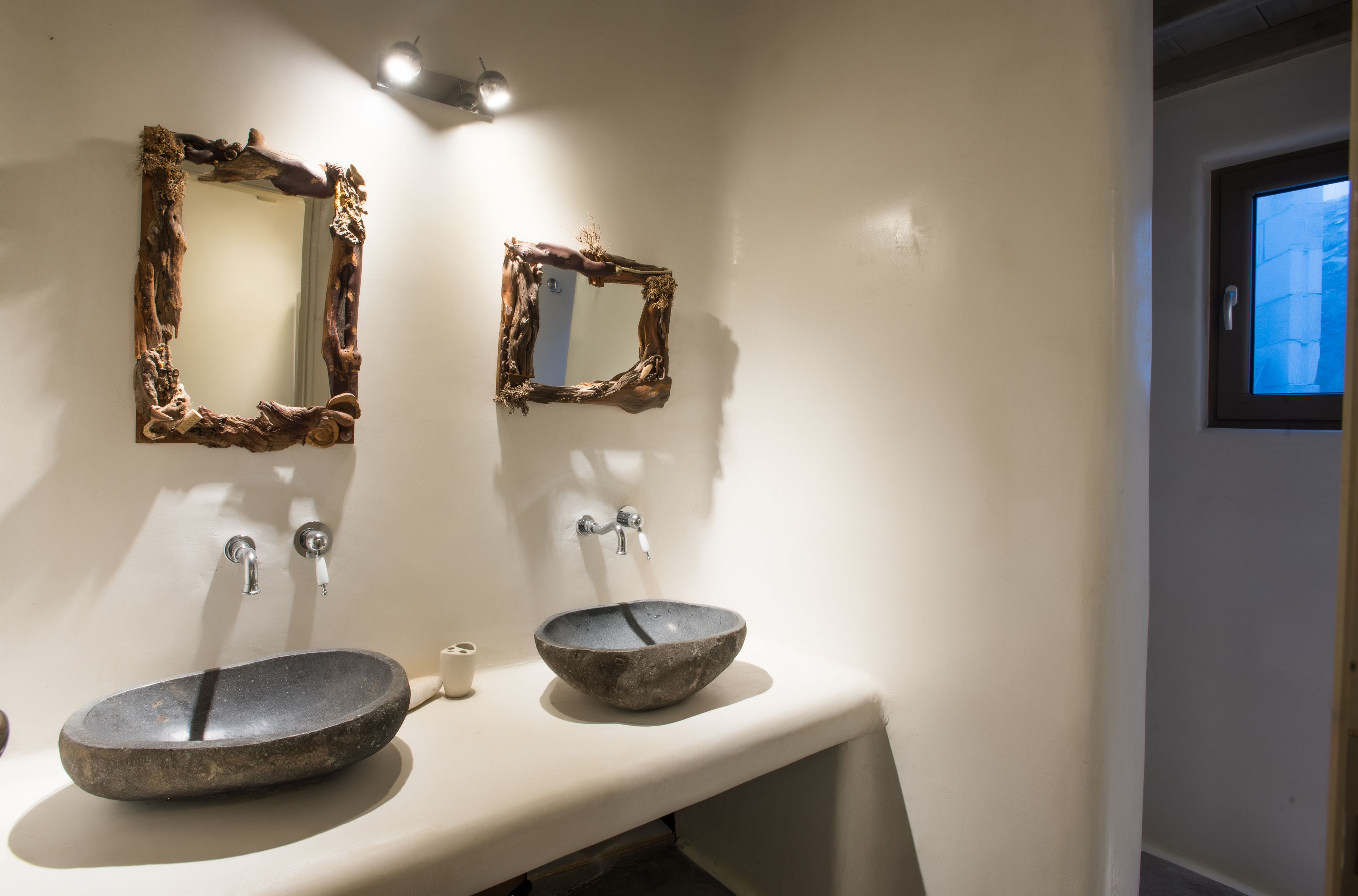 Un baño con dos lavamanos de piedra, un espejo con marco rústico y una ventana pequeña.