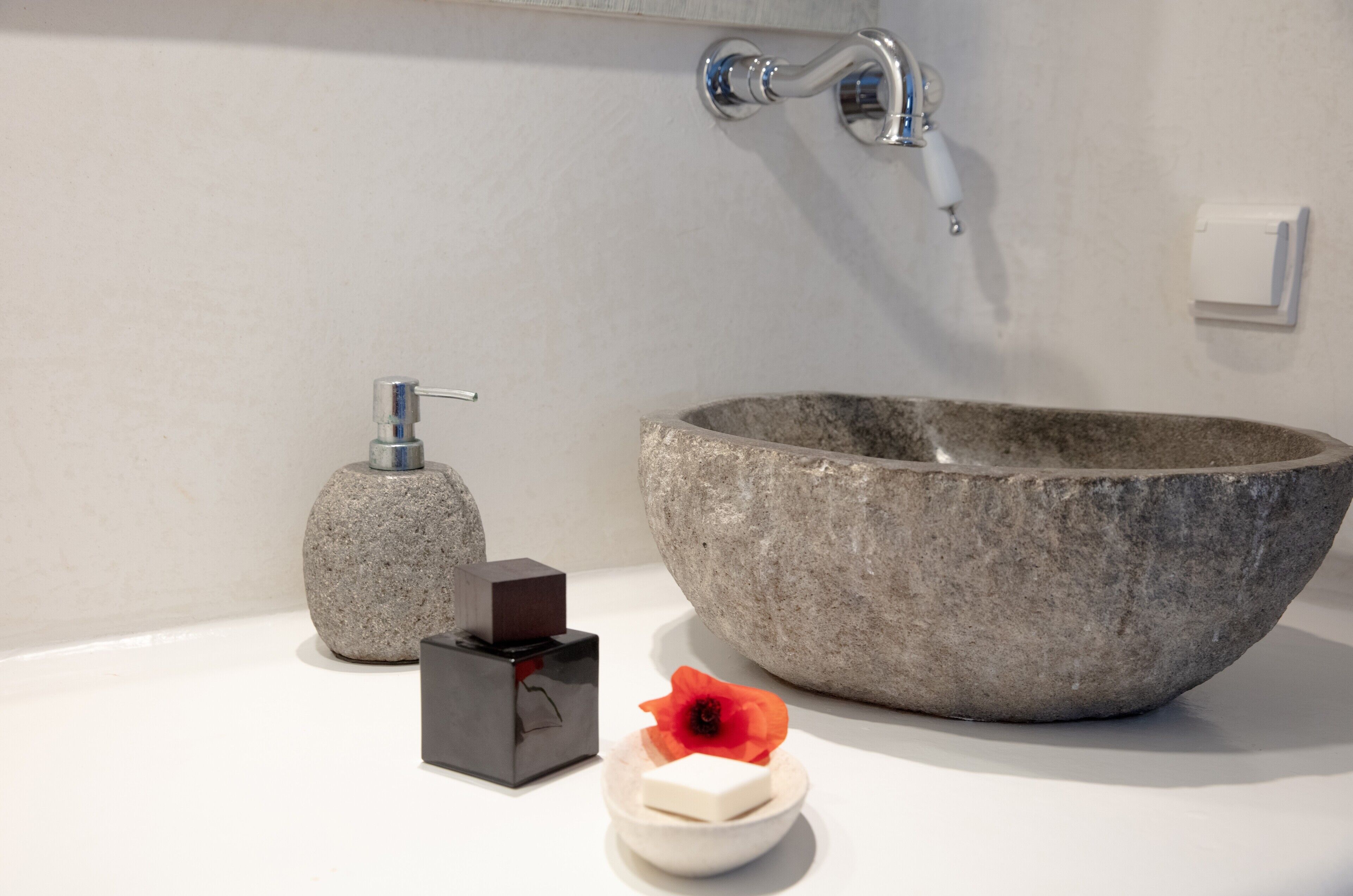 Een badkamer met een stenen wastafel, een zeepdispenser en een klein zeepbakje met een bloem.