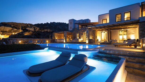 A modern pool area with lounge chairs and a stone wall. - Amallini Suites Mykonos (Mykonos)